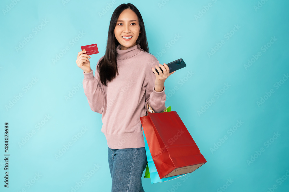 Beautiful Asian woman holding paper shopping bags and showing credit card with smartphone on blue background. Beautiful Asian woman holding paper shopping bags and showing credit card with smartphone on blue background.