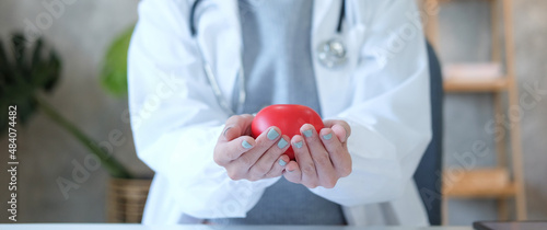 Cropped image of female doctor with stethoscope holding a red heart. Cardiology concept.