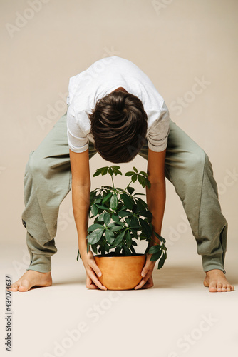 Fotografia, Obraz Boy picking up a potted plant from the floor, bending forward