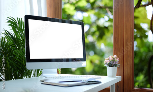 Mockup computer, notebook and flower pot on white table. Blank screen for advertisement text.