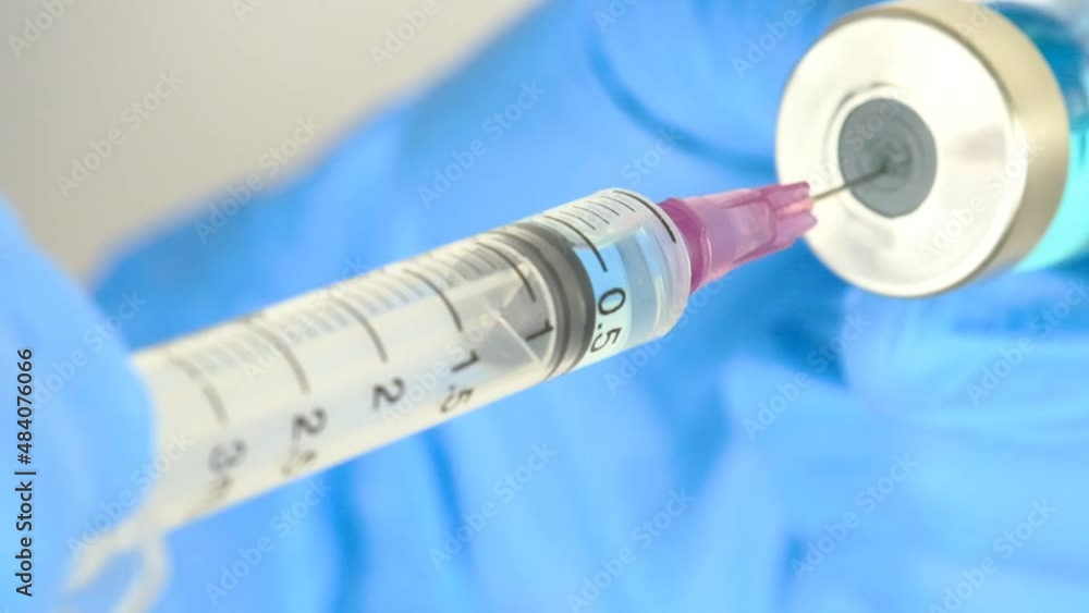 The doctor's hand holds a syringe and a blue vaccine bottle at the hospital. Health and medical concepts. The doctor's hand holds a syringe and a blue vaccine bottle at the hospital. Health and medical concepts.