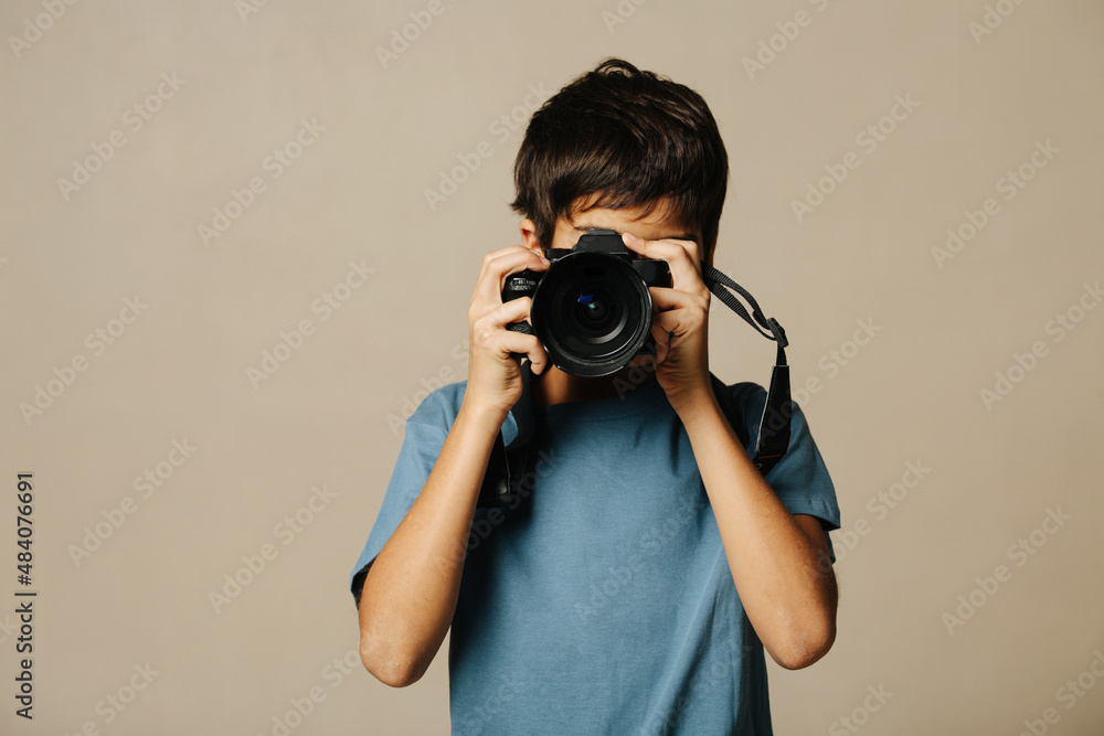 Indian boy taking a photo with a digital camera over beige background. Indian boy taking a photo with a digital camera over beige background.