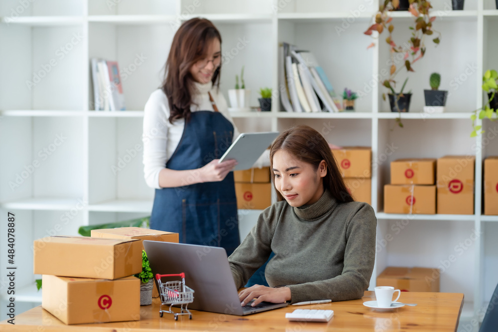 Two beautiful young Asian business owner woman prepare parcel box and check online orders of product for deliver to customer. Shopping Online concept. Two beautiful young Asian business owner woman prepare parcel box and check online orders of product for deliver to customer. Shopping Online concept.