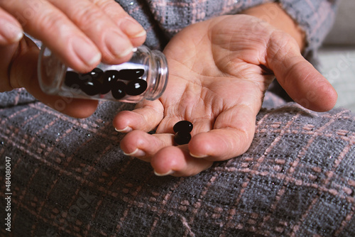 Elderly caucasian woman spilling out black tablets. 