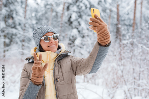 Happy woman making selfie with smartphone in beautiful snowy winter forest photo