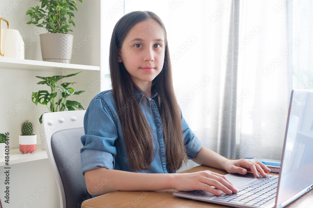 Brunette dressed in a denim shirt is studying at the computer at home, studying, doing her homework, communicating on the network. Looking at the camera Brunette dressed in a denim shirt is studying at the computer at home, studying, doing her homework, communicating on the network. Looking at the camera