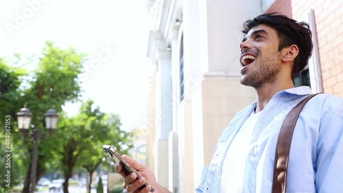 Cheerful happy handsome man in casual wear using smartphone app for virtual communication, holding phone in hand to talking and laughing with his friends. Business communication outside concept