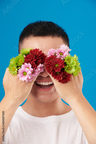 Portrait of happy excited young man holding beautiful blooming flowers in front of eyes photo