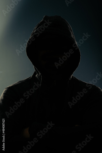Mystery man with hidden face in a hood in the dark.