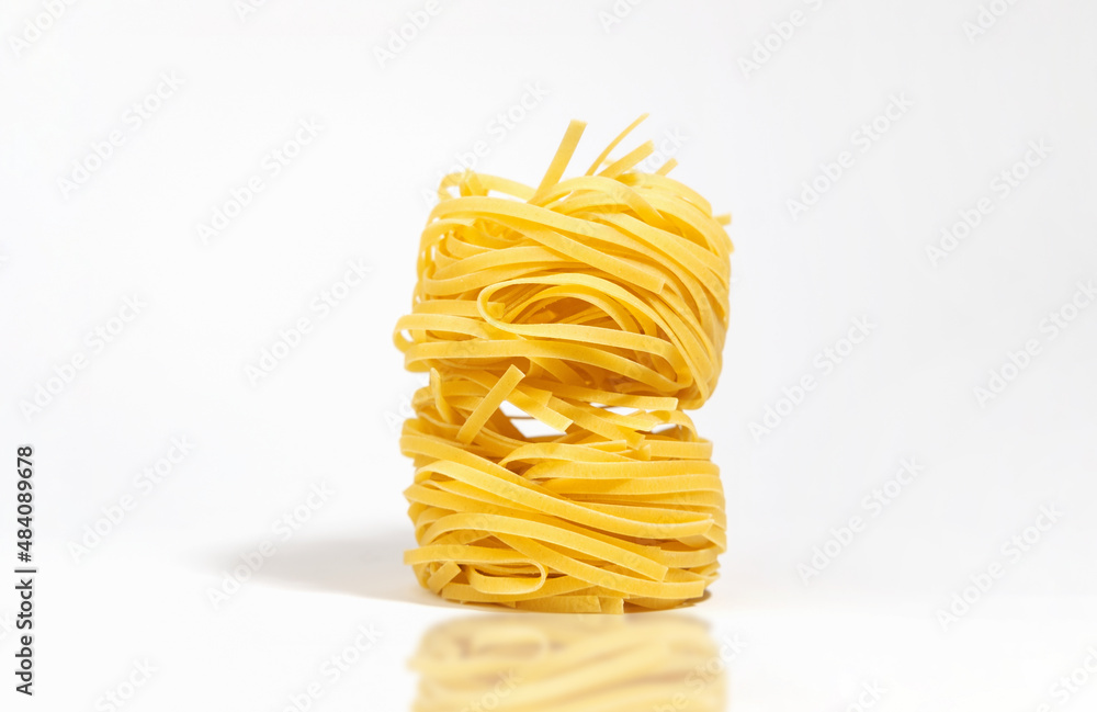 Italian pasta. Spaghetti Capellini, in the form of a tower, isolated on a white background with hard shadows and reflection. Pasta in the form of nests. Creative photo of pasta.