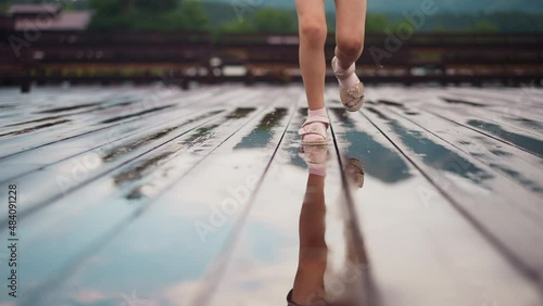 Little child in sandals and pink socks runs to camera and stamps feet in small puddles on empty wooden deck under dribble closeup slow motion