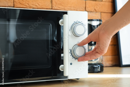 Woman using microwave oven on counter near brick wall in kitchen