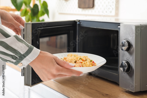 Woman putting plate of rice with vegetables into microwave oven in kitchen photo