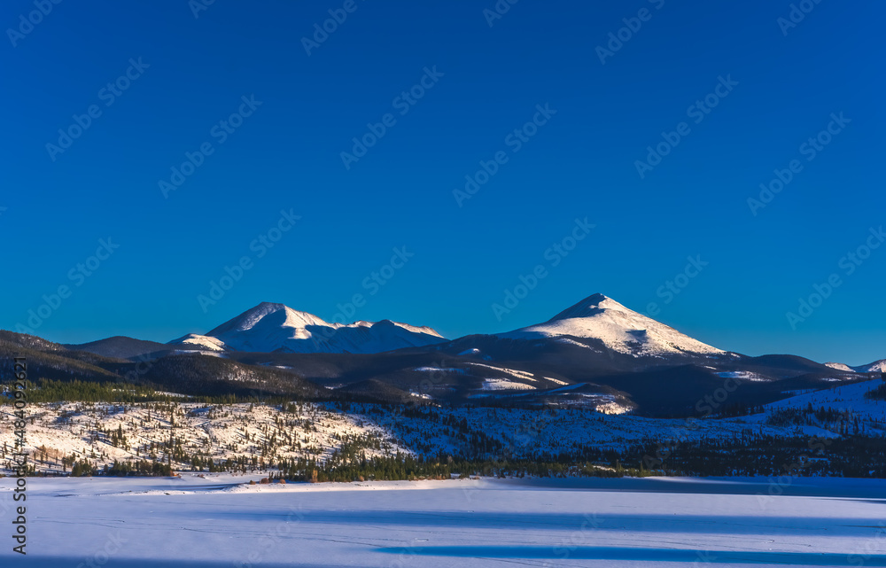 Beautiful view of Colorado mountain peaks with frozen lake in foreground; long shadows on the lake and the mountains; blue hour