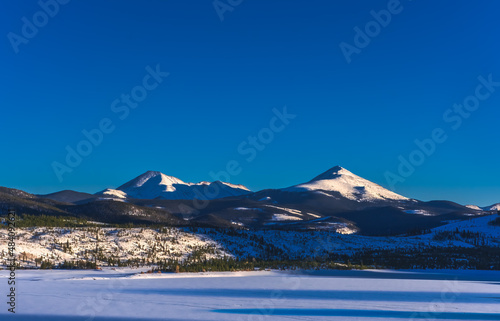 Beautiful view of Colorado mountain peaks with frozen lake in foreground; long shadows on the lake and the mountains; blue hour