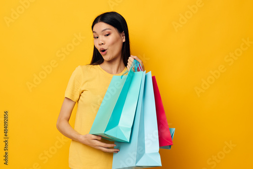 Charming young Asian woman in a yellow T-shirt with multicolored shopping bags studio model unaltered