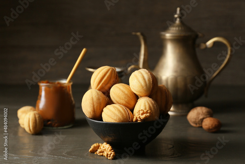 Bowl of tasty walnut shaped cookies with boiled condensed milk on dark wooden background