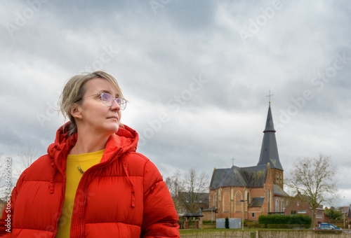 Woman in a red jacket. Portrait against an old catholic church and cloudy sky photo