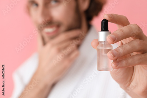 Young man with cosmetic serum on color background, closeup