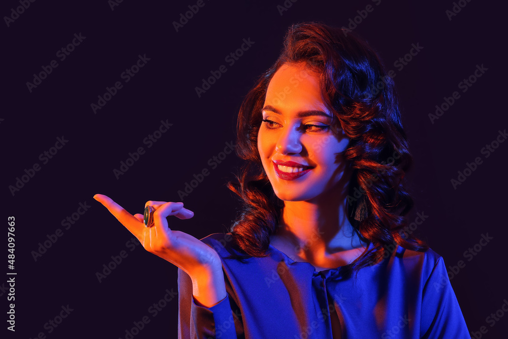 Fototapeta premium Beautiful woman pointing at something on dark background