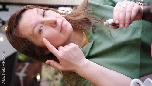 Long-haired woman woman applying glitter on her face. Casual lifestyle. Slow motion, vertical format photo