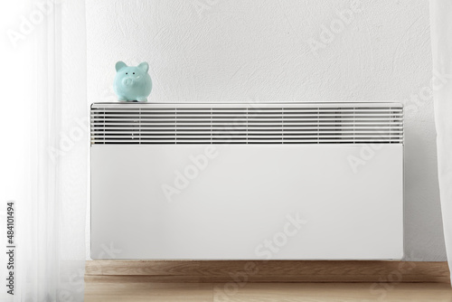 Piggy bank on radiator near white wall. Concept of heating season