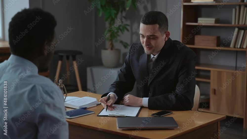 Two business partners discussing contract and sitting at table with laptop in modern office spbas. Young multi-ethnic men read document and talk with smiles, share experiences or ideas and sit at desk Two business partners discussing contract and sitting at table with laptop in modern office spbas. Young multi-ethnic men read document and talk with smiles, share experiences or ideas and sit at desk