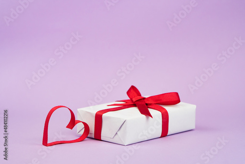 Valentine's Day or birthday concept with copy space. Red ribbon heart and gift box on purple papper photo