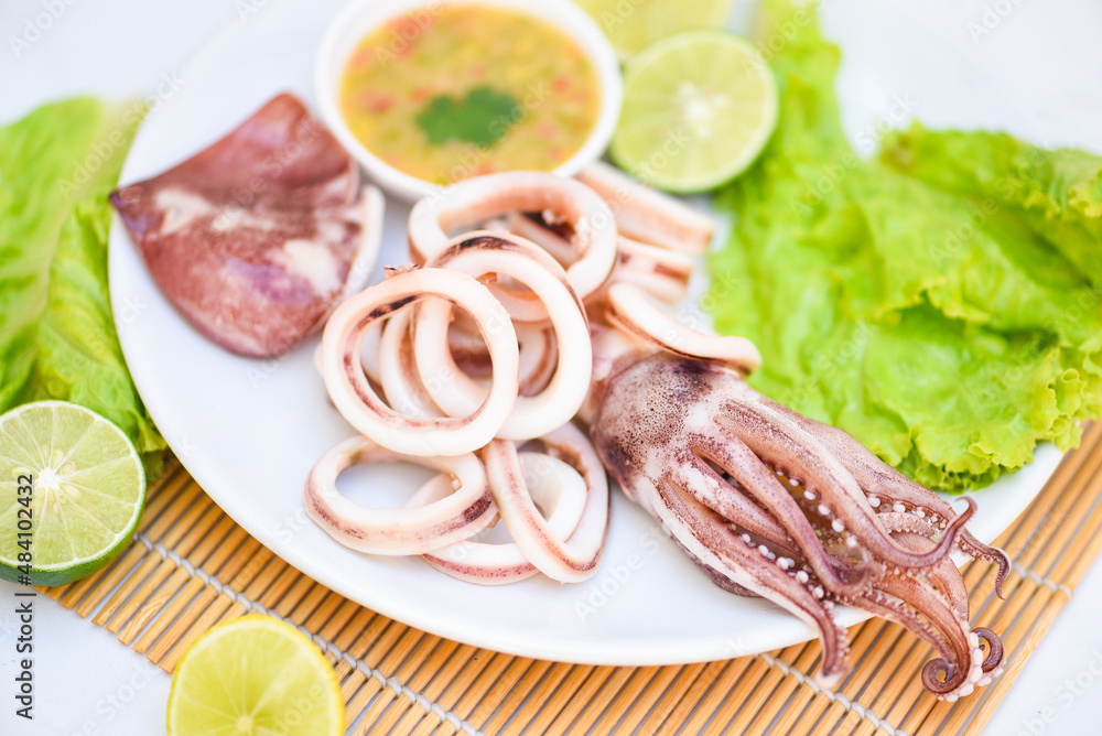 Squid rings on white plate, Fresh squid cooked boiled with lettuce vegetable salad lemon lime and seafood sauce on table background