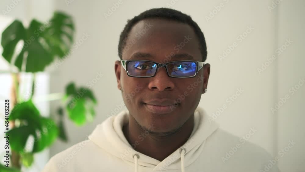 Portrait of young African man smiling and posing while standing in home interior spbd. Close-up view of American guy looks forward with toothy smile and poses for camera, stands in light living room Portrait of young African man smiling and posing while standing in home interior spbd. Close-up view of American guy looks forward with toothy smile and poses for camera, stands in light living room