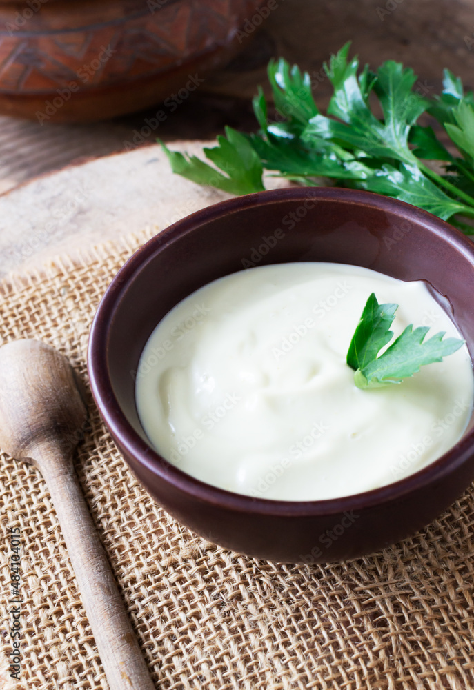 Homemade mayonnaise in a brown bowl with a sprig of green parsley on a wooden table. The concept of proper nutrition. Rustic. Vertical orientation. Homemade mayonnaise in a brown bowl with a sprig of green parsley on a wooden table. The concept of proper nutrition. Rustic. Vertical orientation.