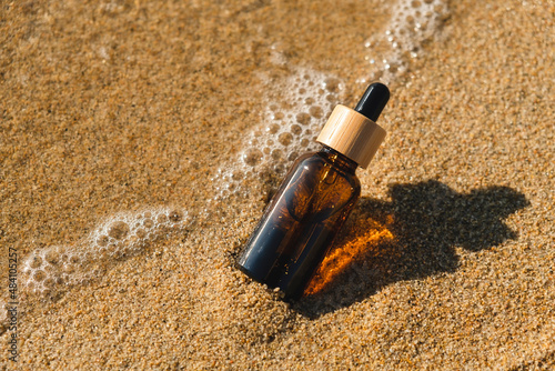 Amber glass bottle with dropper pipette with serum or essential oil on the sea sand. Skin care cosmetic with beautiful shadows. Beauty concept for face body care