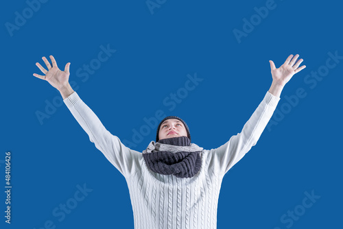 Winter. Snow. A man in a white sweater, scarf and winter hat spread his arms to the side in the snow. Winter clothes