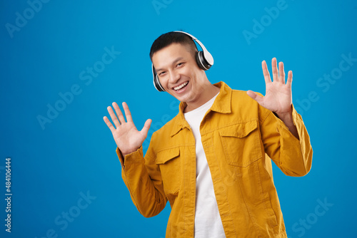 Portrait of joyful young man in headphones listening to good music in headphones, isolated on blue photo