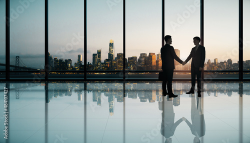 Young european businesspeople shaking hands in modern office interior with panoramic city view and reflections on floor. Meeting, success, teamwork and leadership concept.