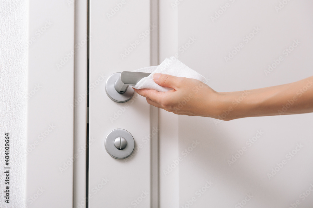 Fototapeta premium Cleaning door handles with an antiseptic wet wipe and gloves. Woman hand using towel for cleaning home room door link. Sanitize surfaces prevention in hospital and public spaces against corona virus.