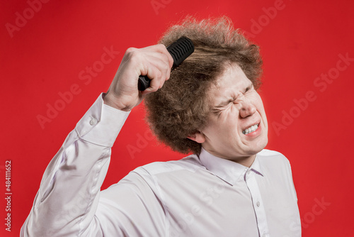 Salon. Comb curly hair. A curly-haired man in a shirt grimaces in pain while combing his hair