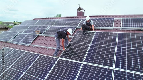 Men workers installing photovoltaic solar moduls on roof of house. Engineers in helmet building solar panel system outdoors. Concept of alternative and renewable energy. Aerial view. photo