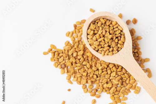 Macro photo of dry yellow fenugreek seeds or shambhala, helba seeds in wooden spoon on white background, top view photo