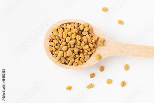Macro photo of green dry yellow fenugreek seeds or shambhala, helba seeds in wooden spoon on white background, top view