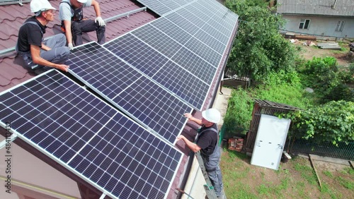 Men workers installing photovoltaic solar moduls on roof of house. Engineers in helmet building solar panel system outdoors. Concept of alternative and renewable energy. Aerial view. photo