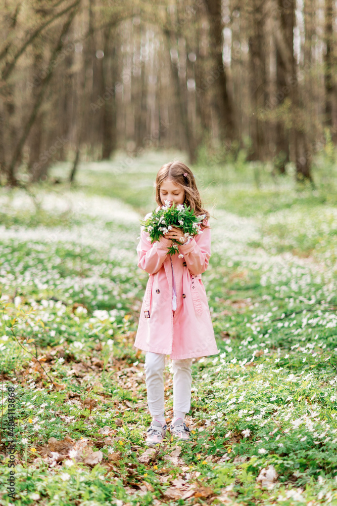 cute girl with a bouquet of snowdrops in the spring forest. A child sniffs flowers cute girl with a bouquet of snowdrops in the spring forest. A child sniffs flowers