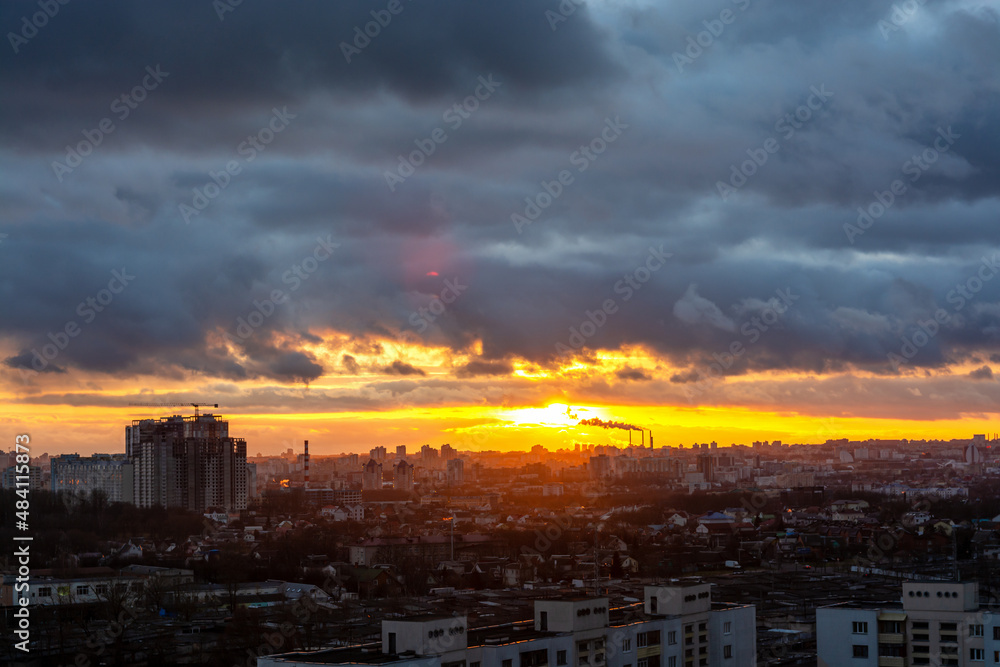 Beautiful sunset sky over the city. The sun over city houses. Blue sky and yellow clouds. Wide panorama.