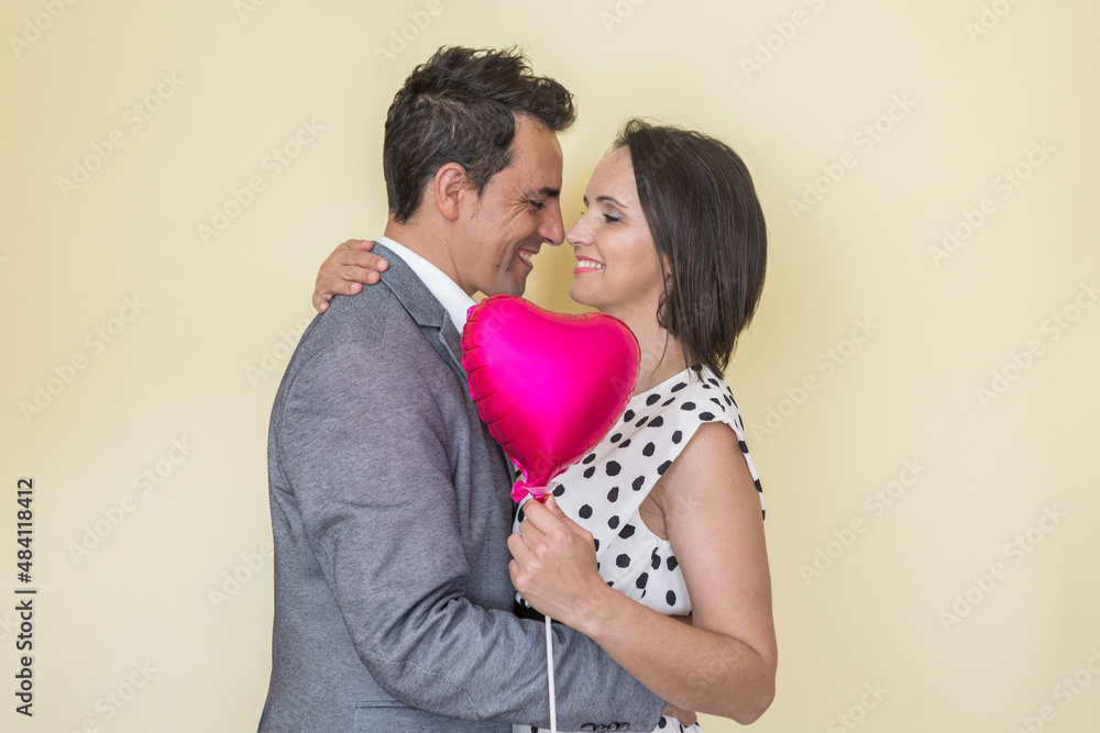 Cheerful Hispanic couple with heart shaped balloon hugging in studio Cheerful Hispanic couple with heart shaped balloon hugging in studio