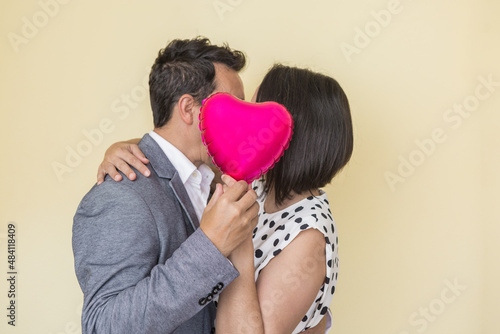 Loving couple kissing and hiding behind balloon