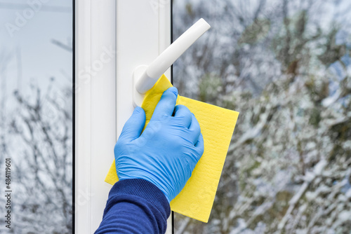 A gloved hand cleans and washes the frame and handle of a white plastic window.