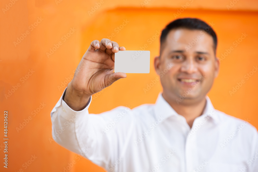 Young Indian man showing blank white card mockup against orange background,Smiling asian guy holding empty business or electronic card for payment, debit,credit, banking, selective focus. Young Indian man showing blank white card mockup against orange background,Smiling asian guy holding empty business or electronic card for payment, debit,credit, banking, selective focus.