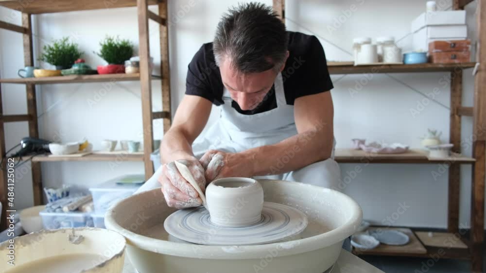 A man works with white clay behind a potter's wheel in a light Scandinavian interior. Hobby, small business. Crafting and Creativity A man works with white clay behind a potter's wheel in a light Scandinavian interior. Hobby, small business. Crafting and Creativity
