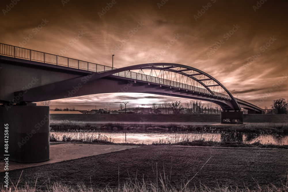 ogromny most nad rzeką i dramatyczne wieczorne niebo z zachodzącym słońcem - obrazy, fototapety, plakaty 