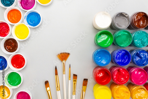 A set of open jars with gouache in different colors and brushes on a gray background. Hobby - drawing. Top view, copy space.